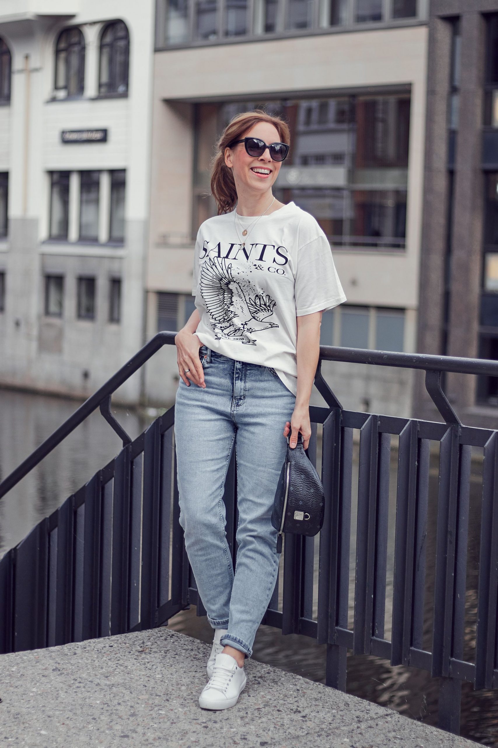 Saints and Co Off-White T-Shirt zu Mom Jeans mit Gürteltasche und Sneakern in weiß.